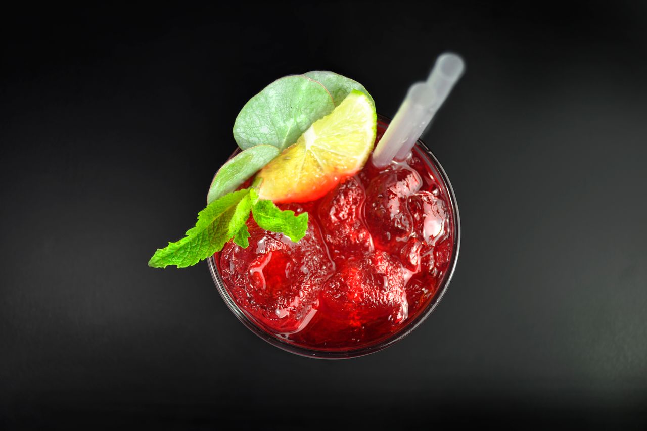 Top view of a vibrant cranberry cocktail with ice, mint, and lime garnish, perfect for summer refreshment.