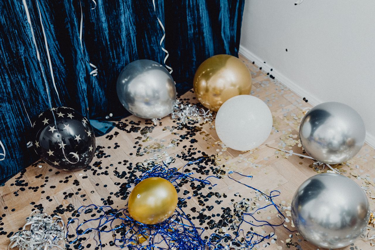 Festive arrangement with gold, silver balloons and confetti on wooden flooring.