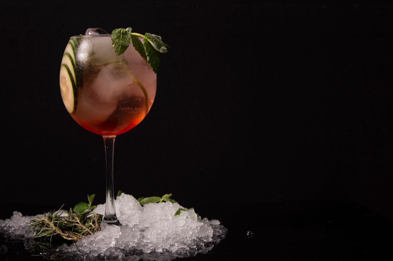 Chilled cocktail with cucumber and mint, served in a glass with ice against a dark background.