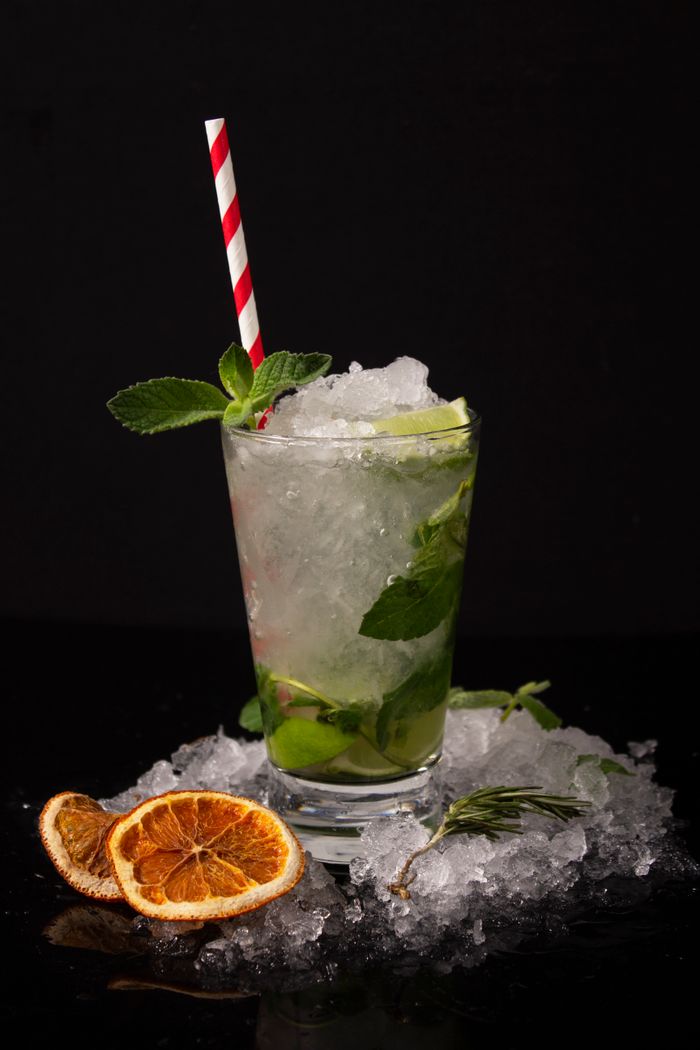 A vibrant mojito cocktail garnished with mint, lime, and a striped straw on ice.